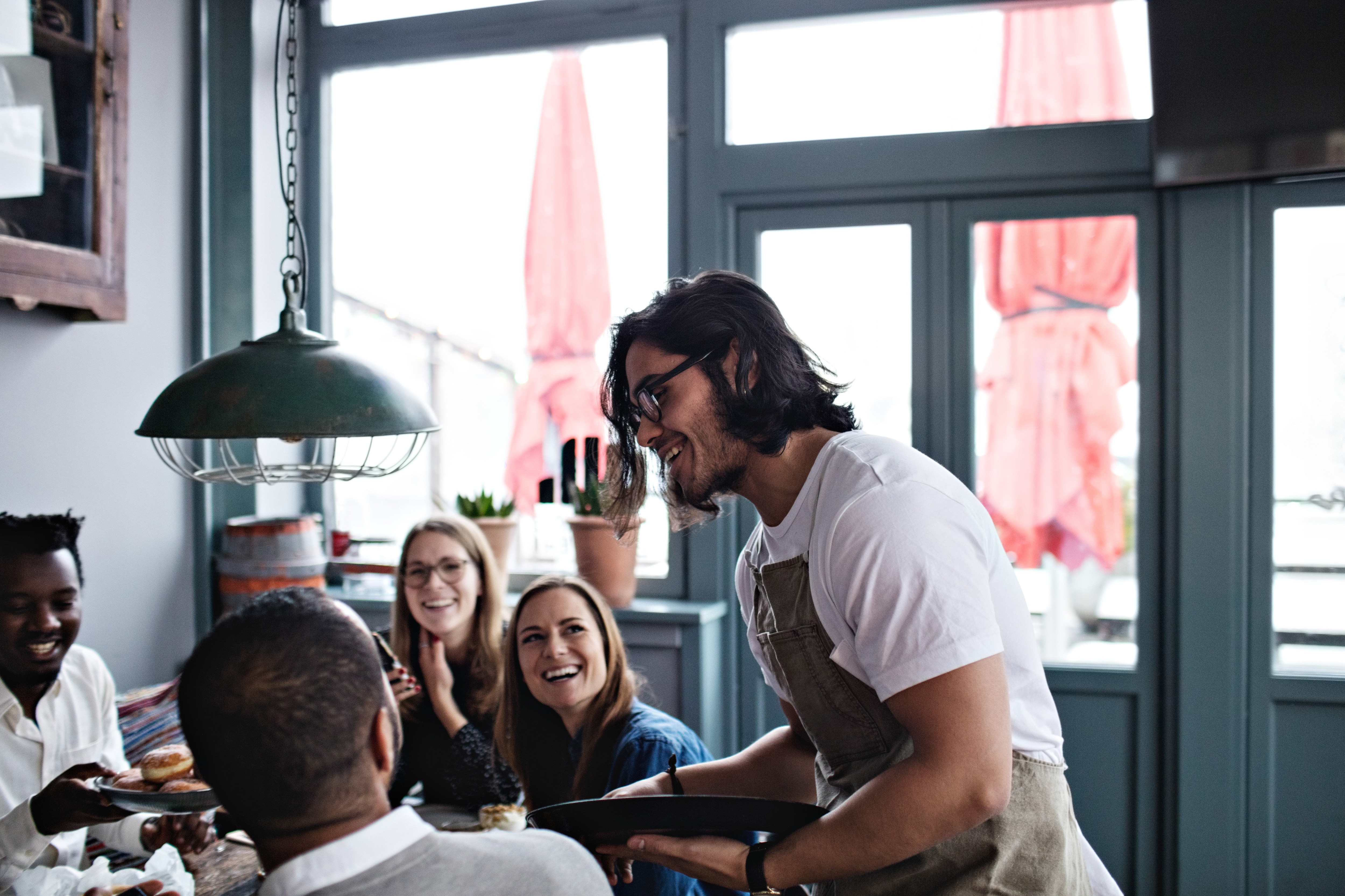 4 people sitting down at a restaurant with a waiter talking to them