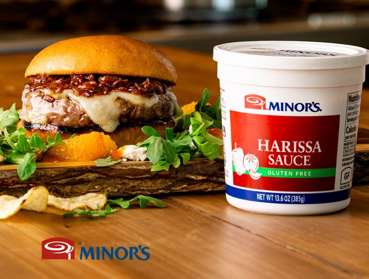 cheeseburger on wood surface with tub of harissa sauce