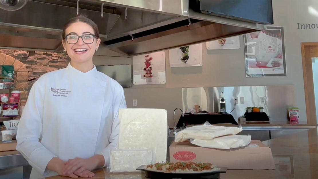 Chef Jordan standing in chef coat leaning on wooden table