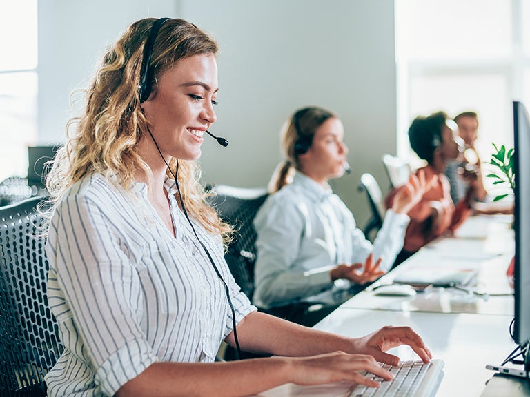 women sitting at long table with headsets and laptops