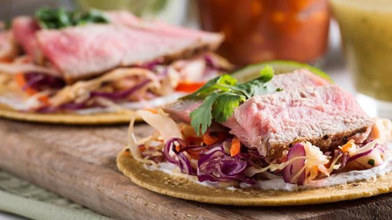 Wooden platter of fish tacos with sides of salsas