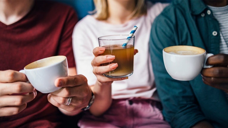 men and a woman holding hot and iced coffee in a cup and mug