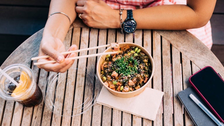 person at table using chopsticks to eat an entree in a bowl