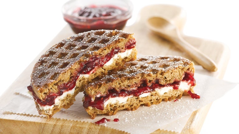 cut sandwich on wooden board with bowl of jam and wooden spoon