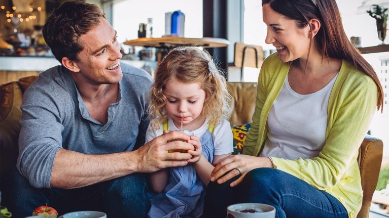 man and woman sitting on couch with girl drinking beverage from straw