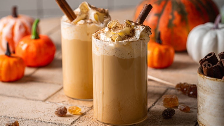 two pumpkin lattes with straws and pumpkins in background