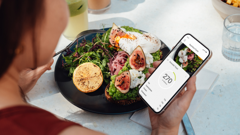 A woman uses her mobile phone app to check nutrition content of a salad with global ingredients.