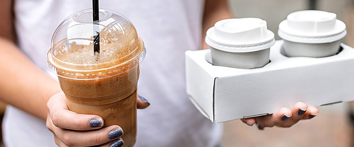 person holding an iced coffee in hand and to-go coffee in another