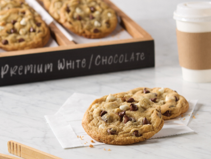 two chocolate chip cookies on a napkin with a box of cookies and a paper cup in background