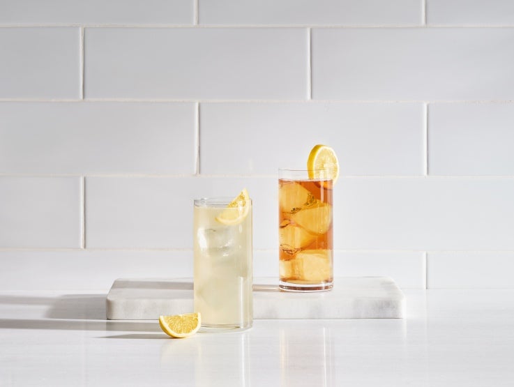 glass of lemonade and iced tea with slice of lemon and lemon wedge