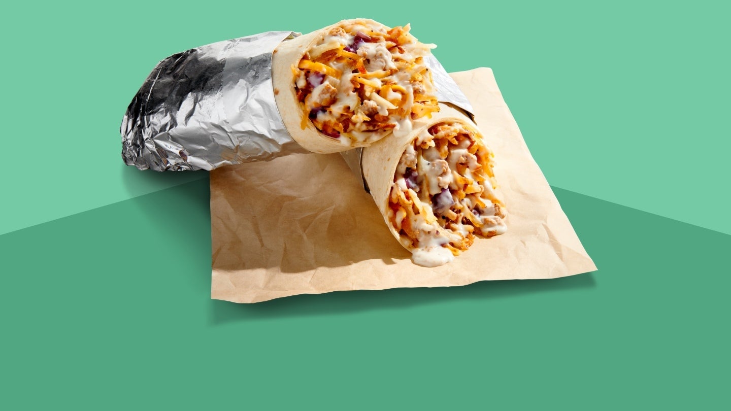 burrito in foil cut in half laying on a paper napkin with green background